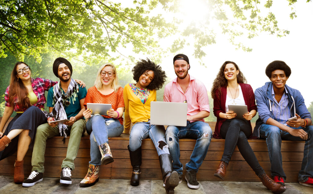 A group of law students sit outside, smiling and holding computers and other devices.