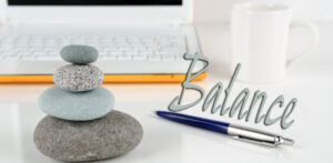 Logo for Balance newsletter, showing balanced meditation rocks in front of a computer, with a pen next to them. 